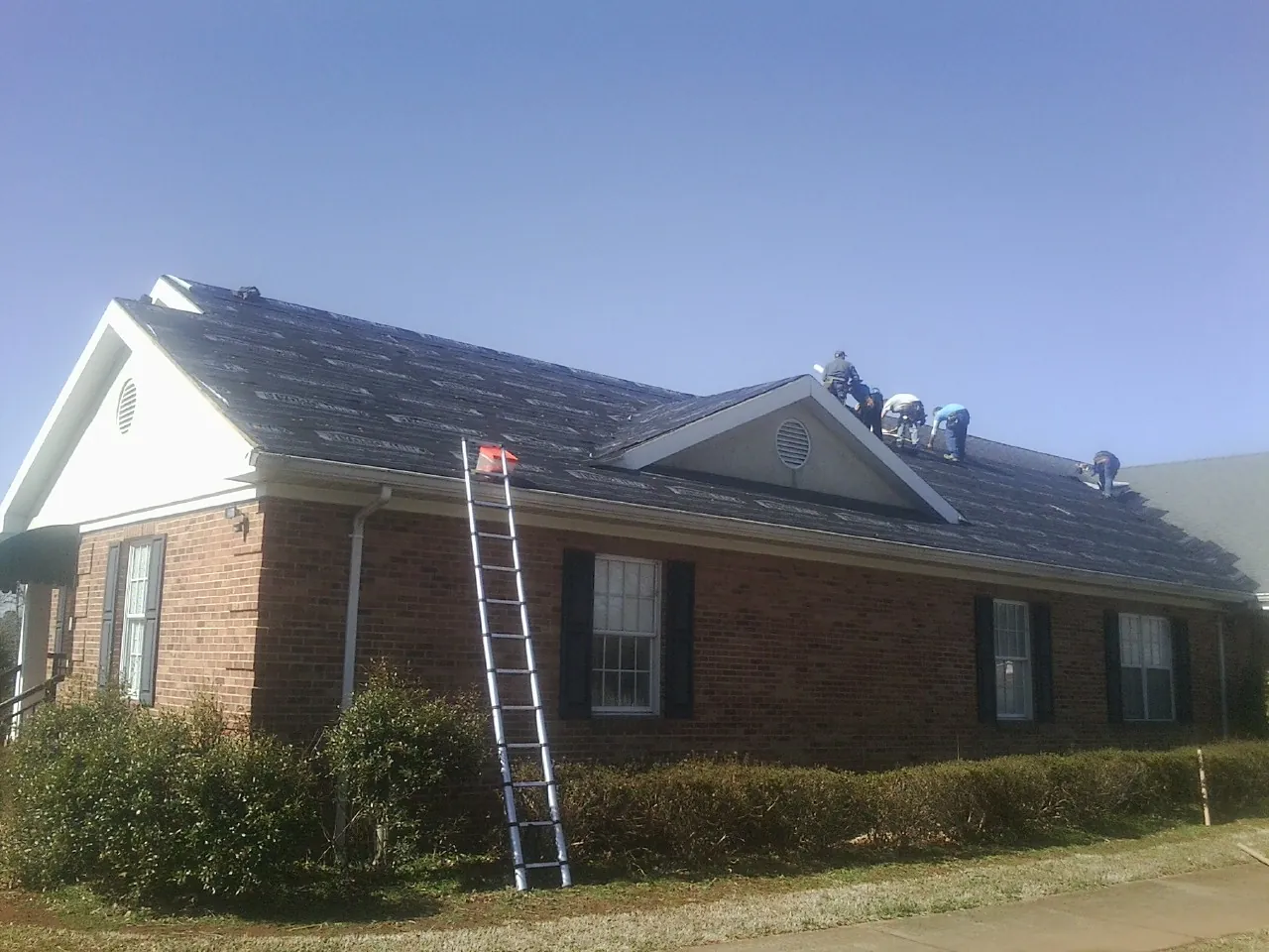 Crew tearing shingles off a brick ranch roof with a ladder set in Edenton