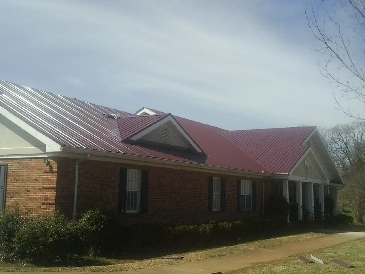 Red metal roof with gabled entries on a long brick building, from a Hail Damage Roof Repair job in Edenton
