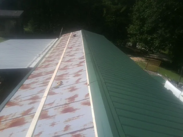 Old rusted panels beside newly installed green metal roofing — Wind Damage Roof Repair by Roofing Brothers in Edenton