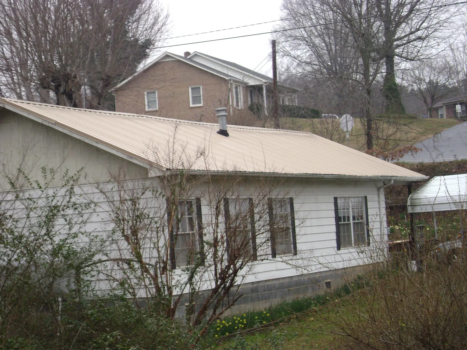 Tan metal roof on a white sided house set into a hillside — Commercial Roofing by Roofing Brothers in Edenton
