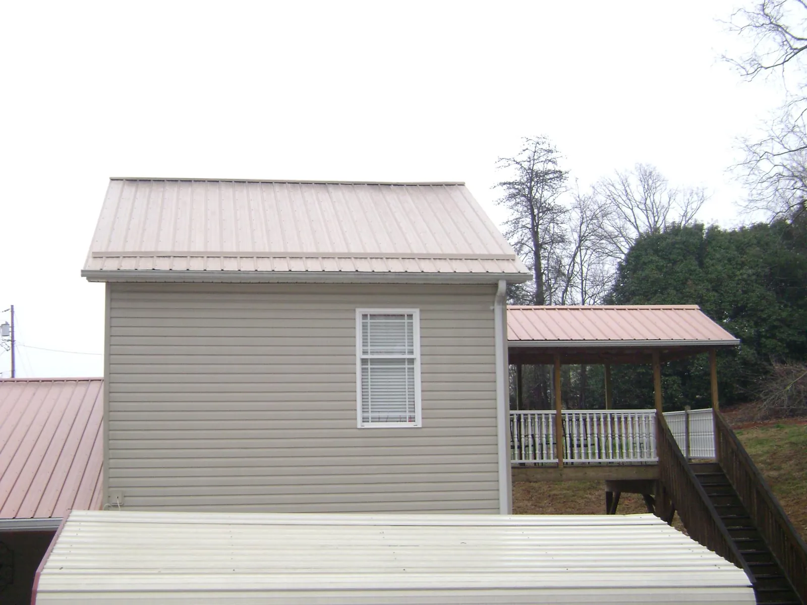 Tan metal roofs on a two story addition and attached porch, from a Roof Replacement job in Edenton